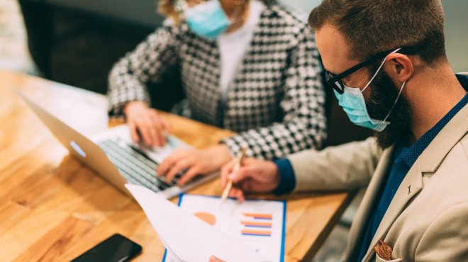 Mann und Frau mit Gesichtsmasken arbeiten am Tisch
