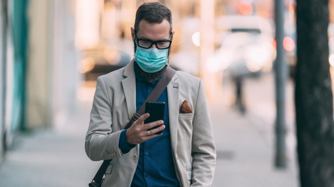 Mann mit Atemmaske schaut auf sein Smartphone