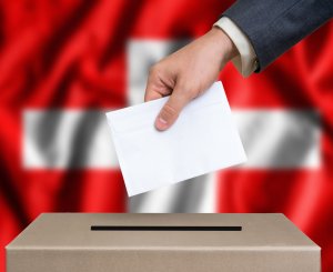 Hand fügt Brief in Urne, Flagge im Hintergrund