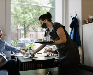 Frau bedient mit Maske einen Mann im Restaurant
